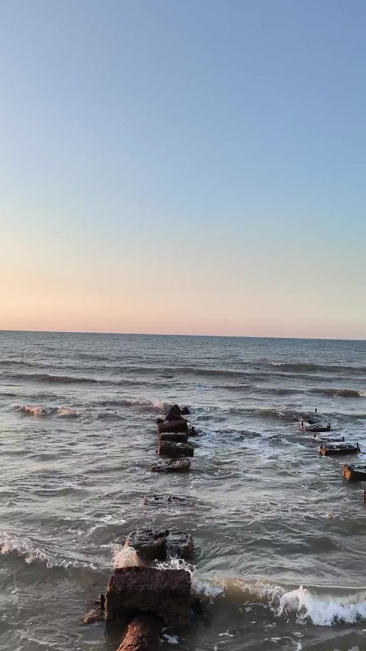 Onde dell'oceano che si infrangono dolcemente contro un vecchio molo di cemento al tramonto.