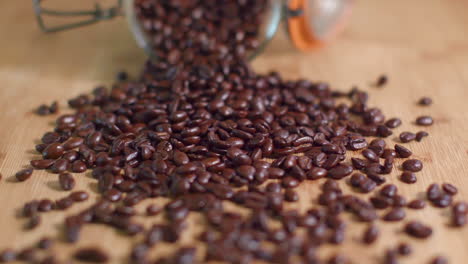 coffee beans spill from mason jar onto wooden surface in slow motion