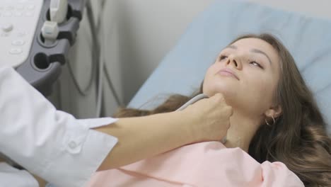 ultrasound scanning diagnostic of young woman thyroid gland in clinic. woman doctor runs ultrasound sensor over patient's neck.