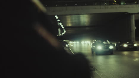 Person-shoulder-night-city-near-highway-road-with-passing-cars.