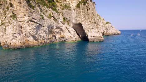 Playa-Oasis-Iluminada-Por-El-Sol-Con-Cuevas-Keri-En-La-Isla-De-Zakynthos,-Barcos-En-Aguas-Cristalinas-Y-Ambiente-Veraniego.