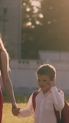happy young woman in red dress walks with smiling schoolboys in green park at back sunlight slow motion