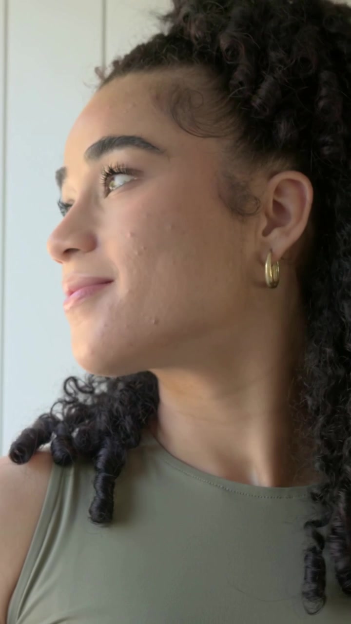Video verticale: Luce a sinistra che attira lo sguardo, donna con top color oliva vicino alla finestra che gira la testa e solleva una tazza per bere.