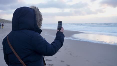 una mujer hace un video con un smartphone en un día ventoso en la hermosa playa de sylt