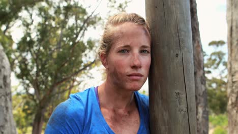 portrait of fit woman leaning on wooden pole during obstacle course