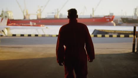 silueta de un trabajador en uniforme naranja caminando por el almacén del puerto junto al mar durante su descanso y levantando las manos