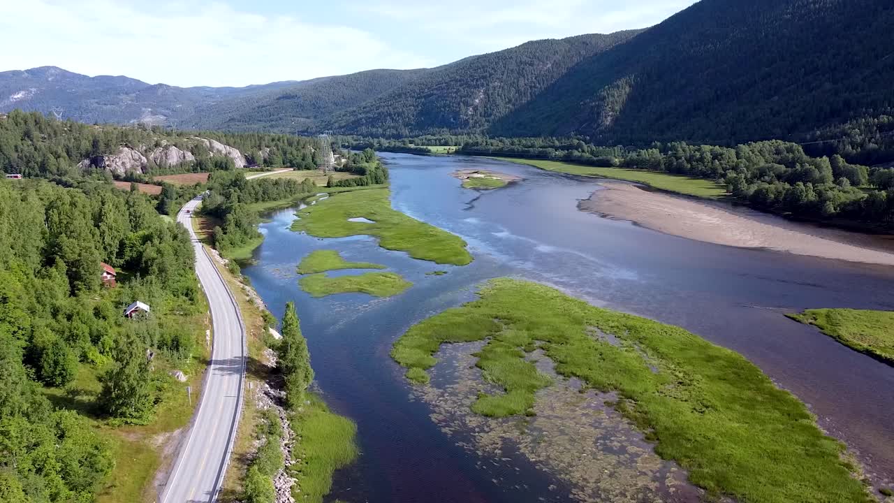 Dronekuvaa viehättävästä norjalaisesta maisemasta, jossa on rehevää vehreyttä, mutkitteleva joki ja ympäröiviä vuoria kirkkaan taivaan alla