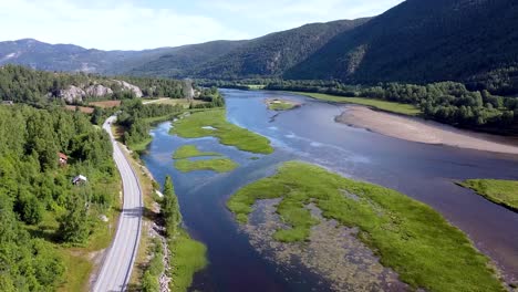 imágenes de drones que muestran un pintoresco paisaje noruego con exuberante vegetación, un río sinuoso y las montañas circundantes bajo un cielo despejado