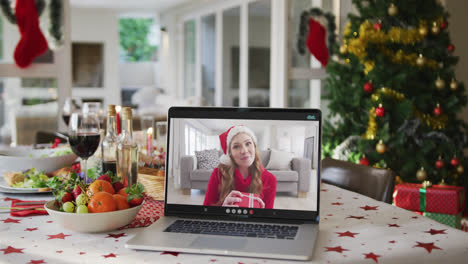 Glückliche-Kaukasische-Frau-Mit-Weihnachtsmütze-Auf-Laptop,-Die-Auf-Dem-Weihnachtstisch-Liegt