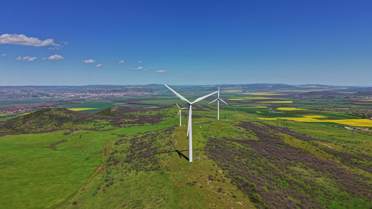 Turbine eoliche su colline sotto un cielo blu di giorno in una zona rurale.