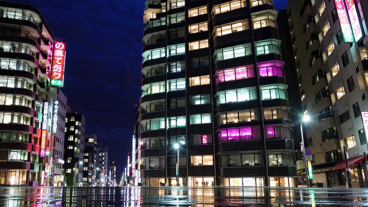 Night cityscape of a Japanese city with illuminated buildings and wet street reflections