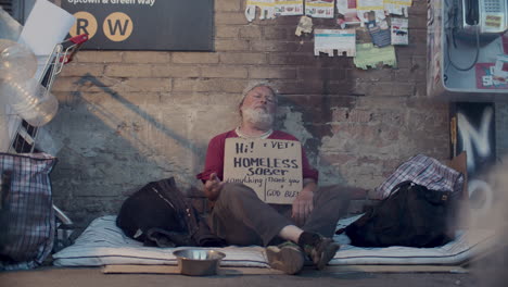 elderly beggar sitting on urban street with cardboard sign asking for money