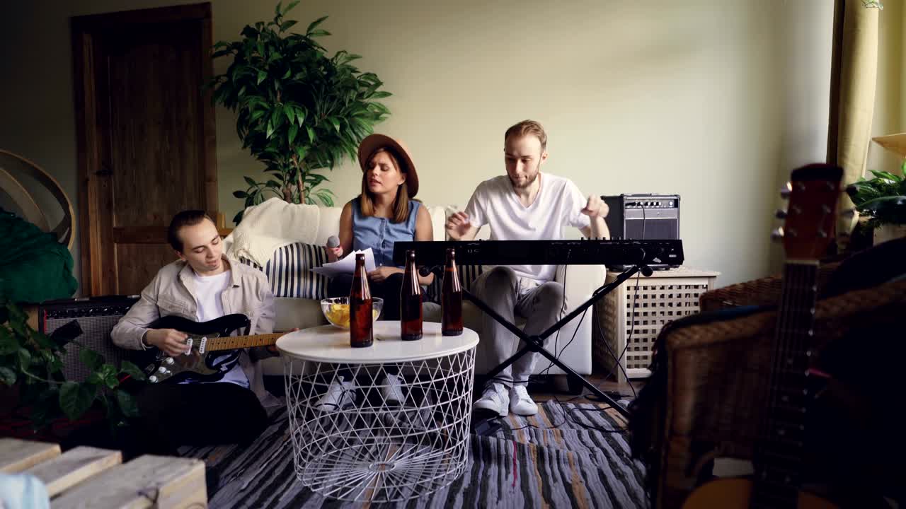Creative friends musical group are having rehearsal, guitarist is playing the guitar, vocalist is singing and keyboarder is adjusting musical instrument.