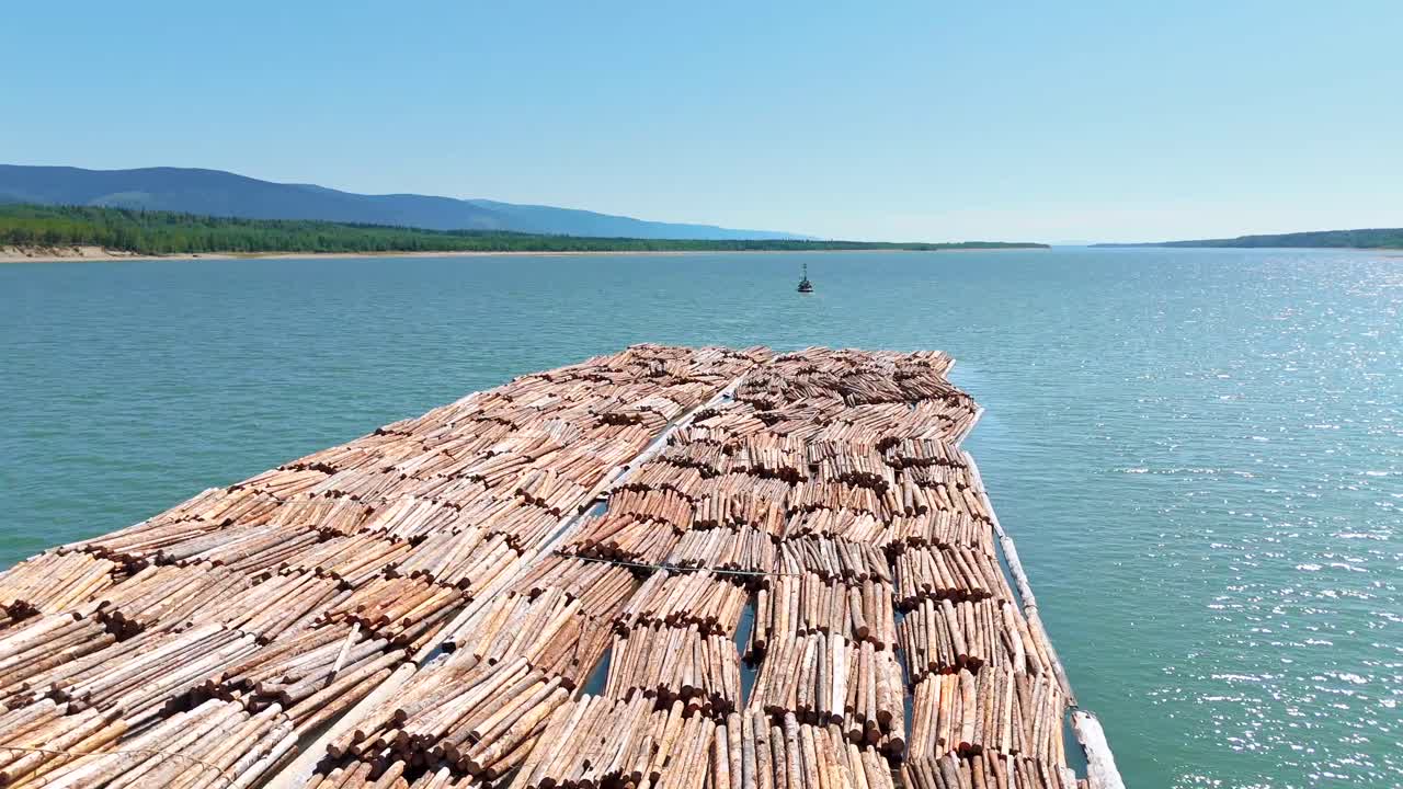 Capture drone footage of a tugboat pulling logs through the remote Canadian wilderness, showcasing the lumber trade’s role in building the economy and fueling global construction.