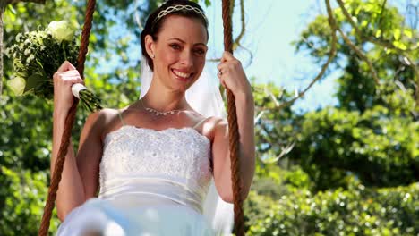novia feliz sentada en un columpio mirando a la cámara