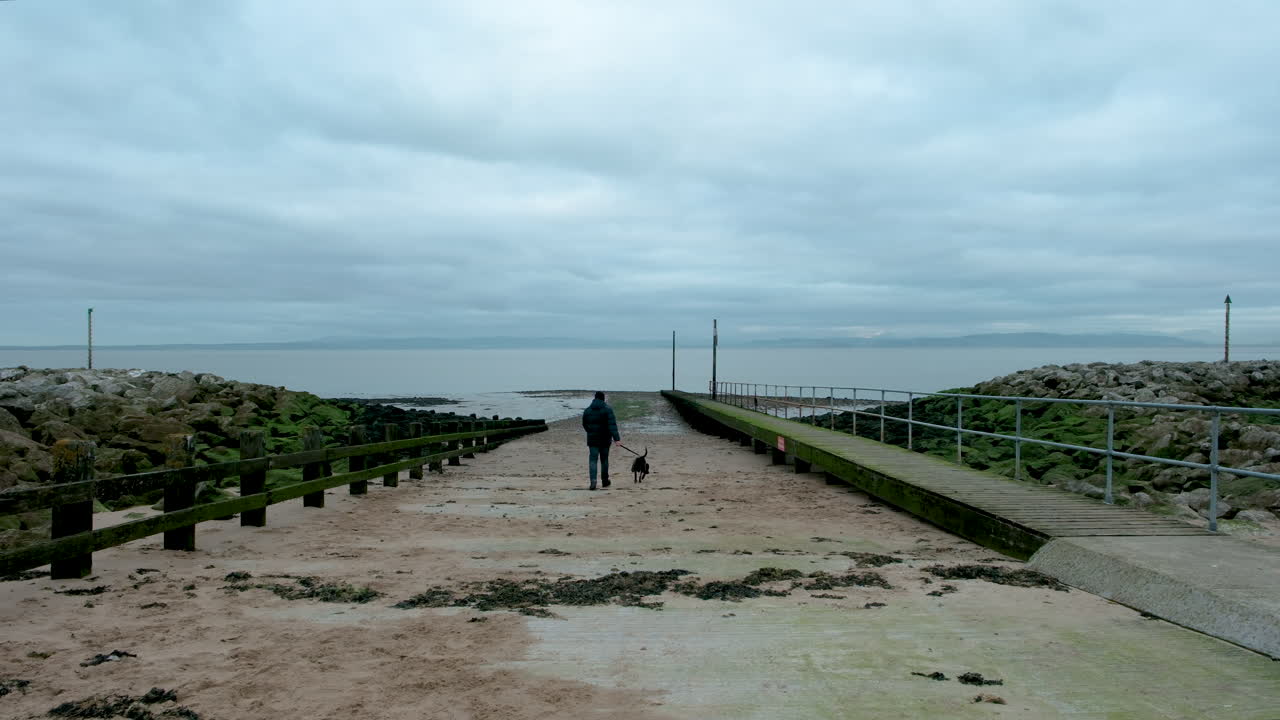 Uomo che porta a spasso il suo levriero lontano dalla spiaggia a Morecambe in una grigia giornata invernale nuvolosa di dicembre