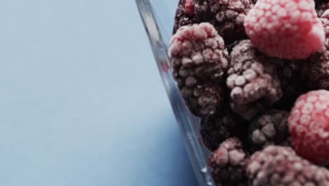 micro video of close up of raspberries in glass bowl with copy space on blue background