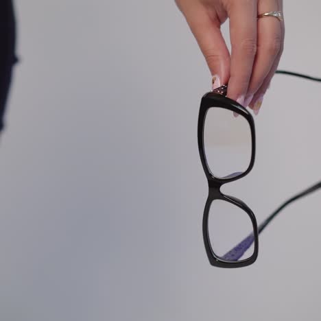 female hand is holding model of eyeglasses with black rim on a gray background