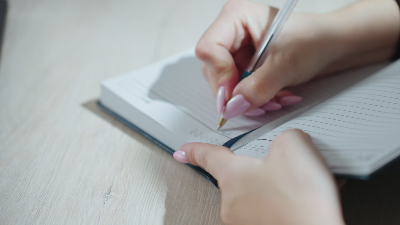 close up of lady with manicured nails flipping open lined notebook on wooden desk, preparing to write with blurred hand motion and ribbon bookmark