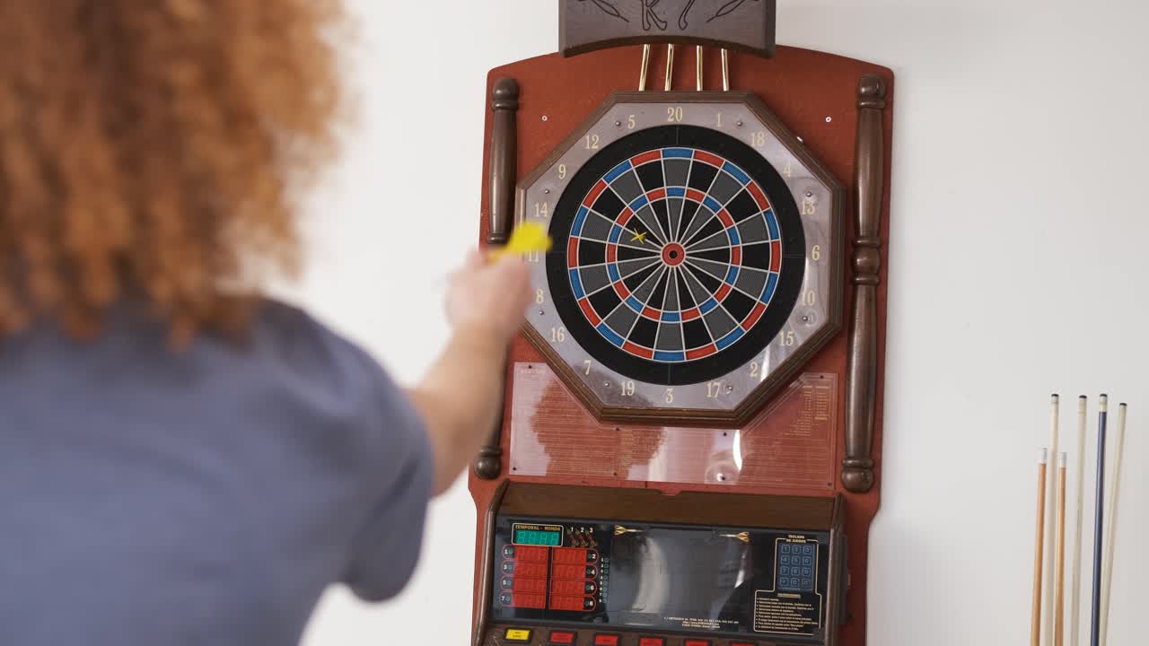 Cheerful man playing game of dart with friends at home