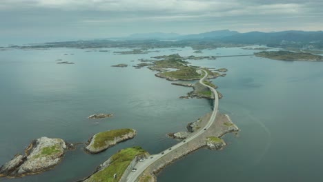 High-angle-grand-view-of-Atlanterhavsvegen-bridge-in-Nordmore,-Norway-with-grassy-islands-as-cars-drive-and-park-in-lot