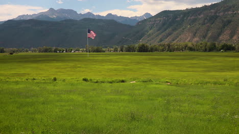 gran bandera americana ondeando con gracia en el viento sobre un campo de hierba con las montañas de san juan en segundo plano