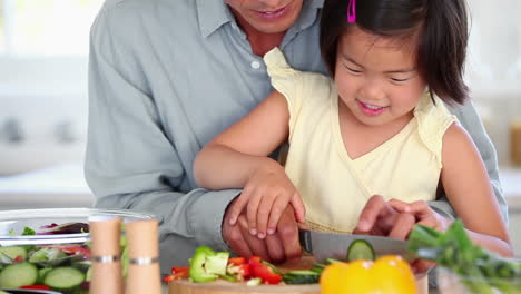 girl cutting a cucumber with her father