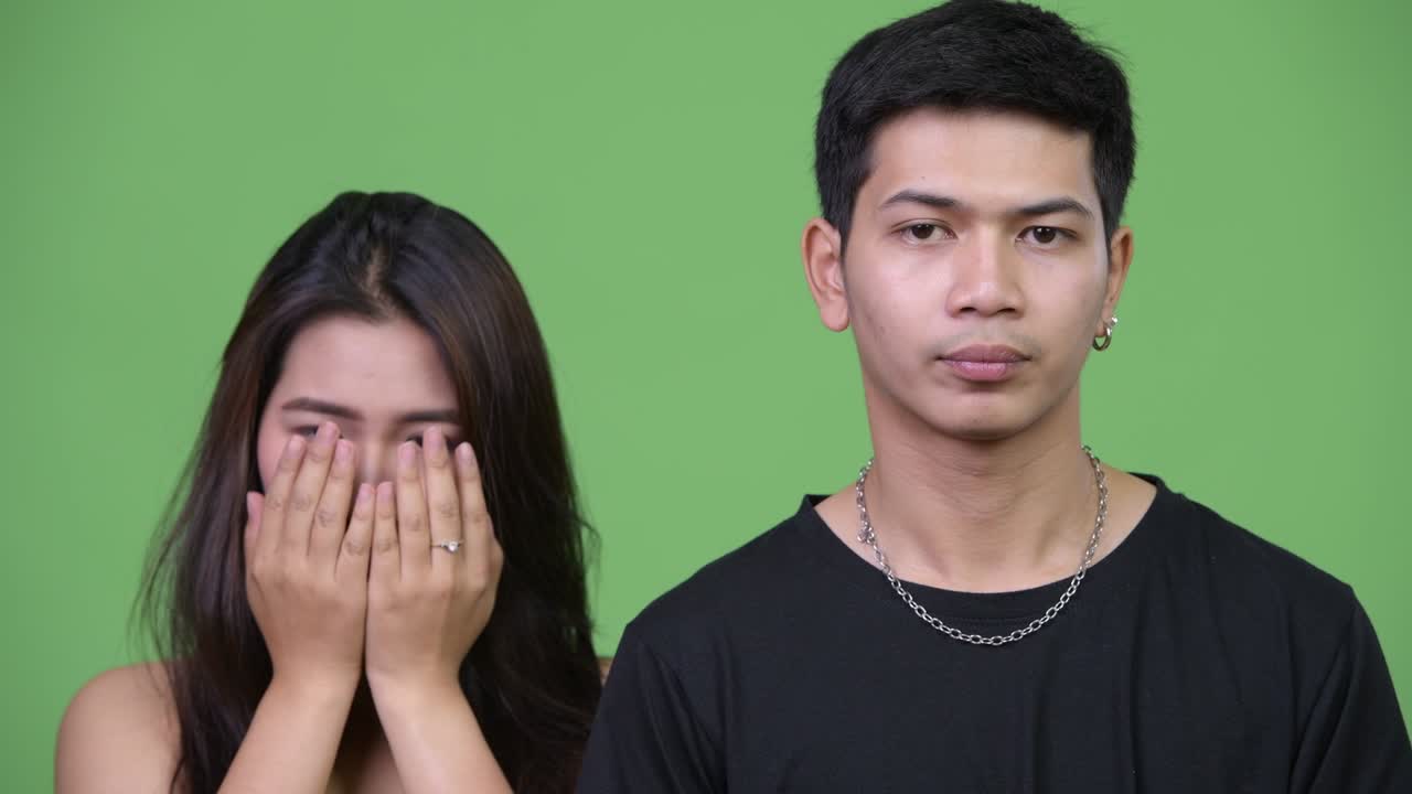 Young upset Asian man with young Asian woman covering face