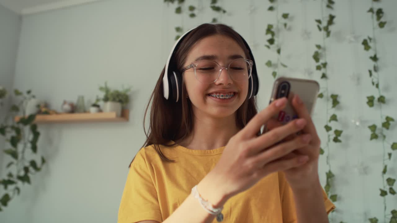 Ragazza adolescente caucasica che balla nella sua stanza con cuffie e telefono.
