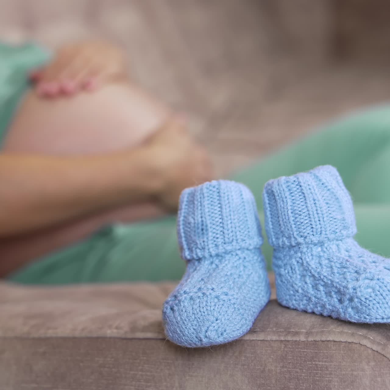 Pregnant woman with a big belly, tummy, laying at the sofa with knitted shoes for the baby. Happy pregnancy, family, parenting, motherhood concept