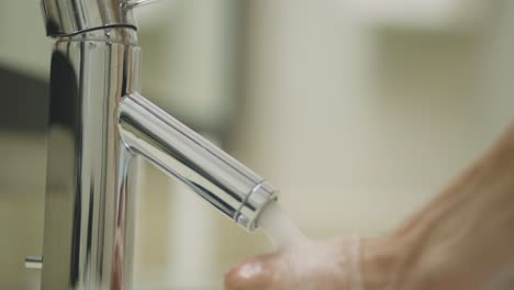 higiene - lavarse las manos con agua corriente bajo el grifo inoxidable y moderno en casa