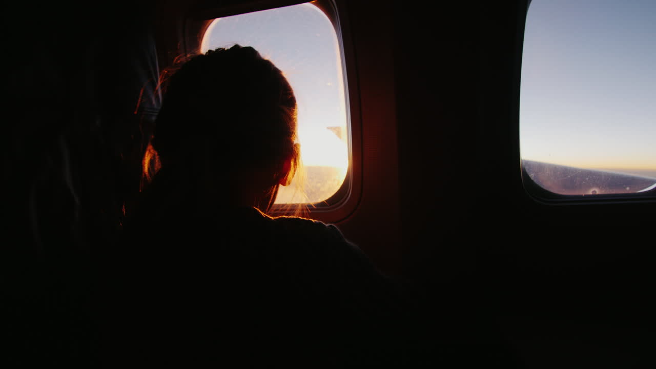 비행기에 앉아 떠오르는 태양을 창밖으로 내다보는 소녀