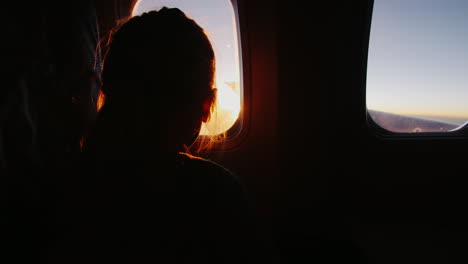 girl sitting in an airplane looking out the window at the rising sun