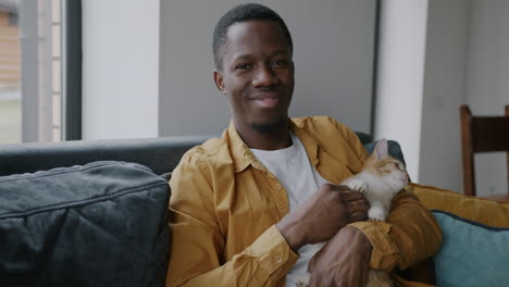 man holding ginger cat on a couch
