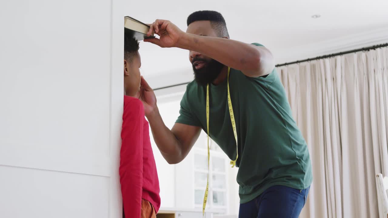 Happy african american father and son measuring height, in slow motion