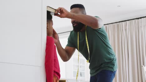 happy african american father and son measuring height, in slow motion