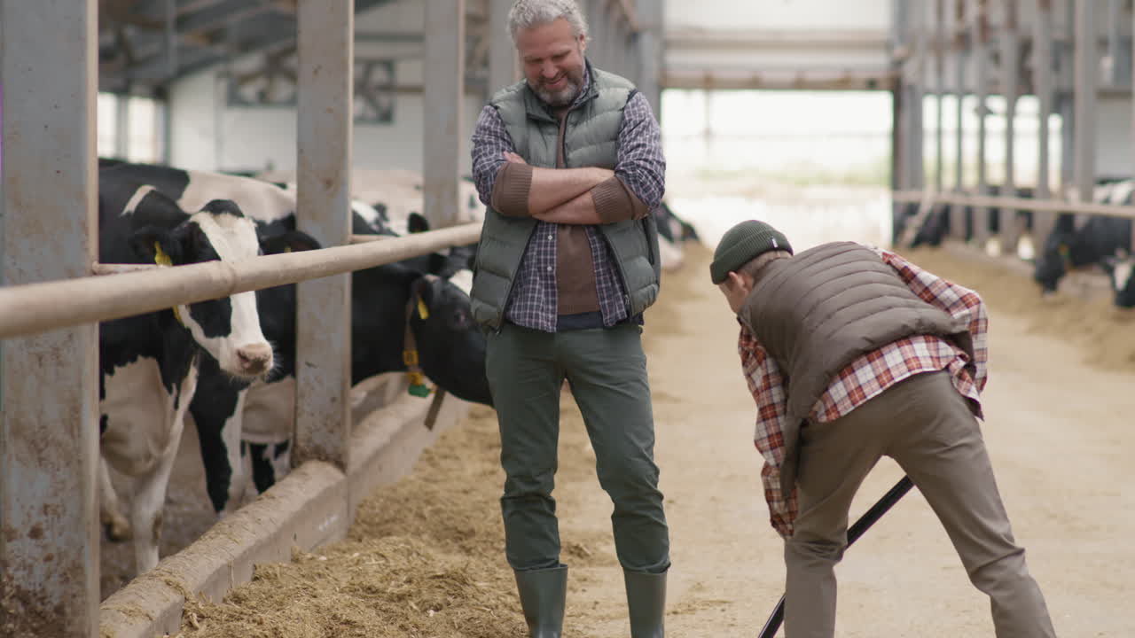Man Overseeing his Teenage Son Work at Dairy Farm