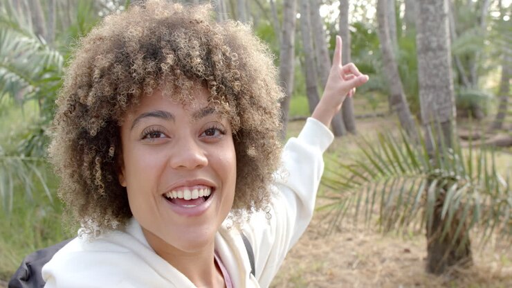 Una giovane donna birazziale con i capelli ricci sorride luminosamente, indicando verso l'alto