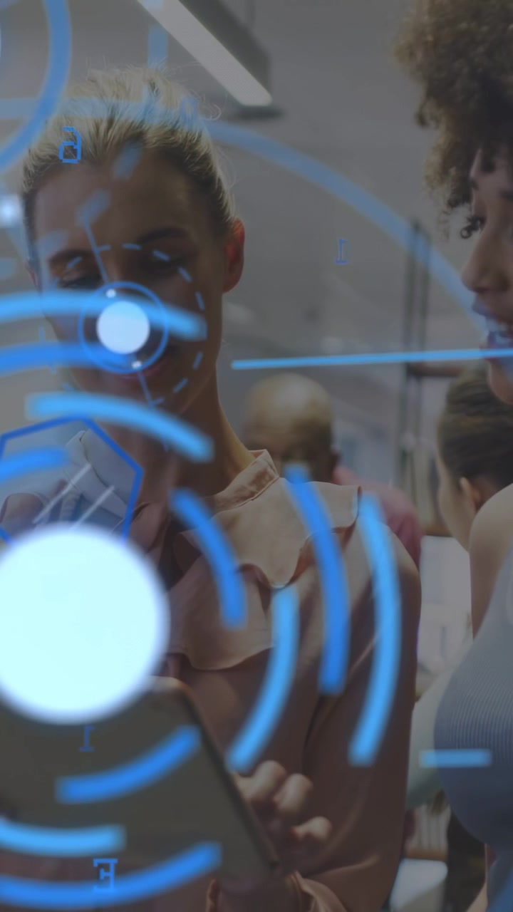Vertical video: Left woman tilting tablet, starting blue UI covering face, peer reviewing in tech