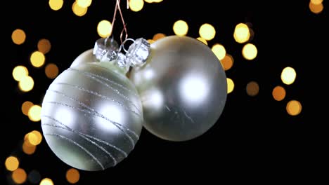 tres adornos de bolas de navidad plateados con luces fuera de foco parpadeando en el fondo, de cerca