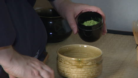 matcha tea is scooped into a tea bowl during a japanese tea ceremony known as "chanoyu