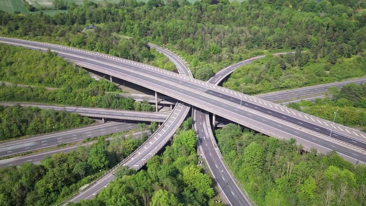 A hyperlapse showing a vast and complex highway interchange with multiple elevated roads weaving through a dense green forest.