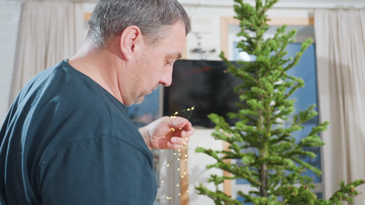 Close-up of aged man carefully straightening Christmas lights on festive tree, preparing for holiday decoration, cozy holiday atmosphere, family home, seasonal decor