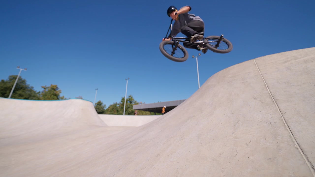 Ciclista BMX che esegue un trick di salto in uno skate park in cemento.