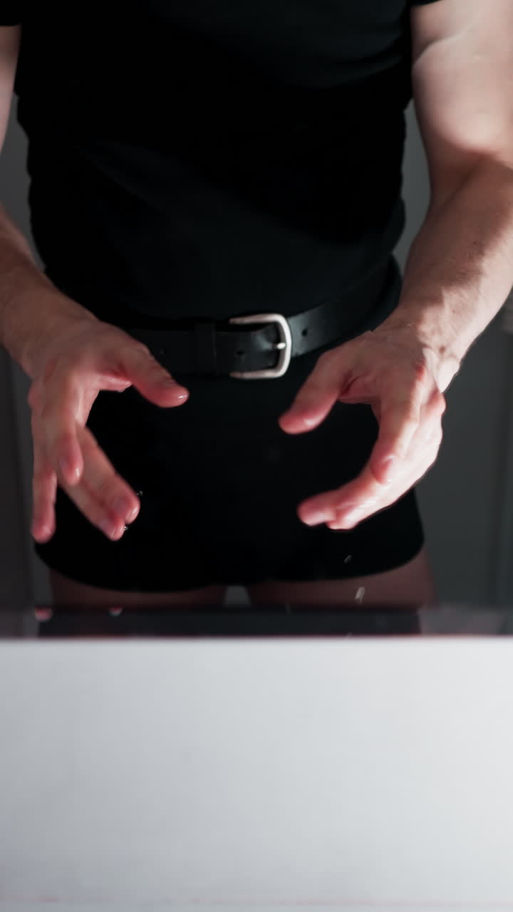 vista en primera persona de una persona en pantalones cortos con un cinturón, reflejada en un espejo del baño, sacudiendo las gotas de agua de las manos después de lavarse