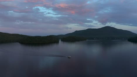 Drone-Siguiendo-Un-Bote-Solitario-En-Un-Lago-Al-Atardecer-Con-Hermosos-Colores-En-El-Municipio-Del-Este,-Quebec,-Canadá