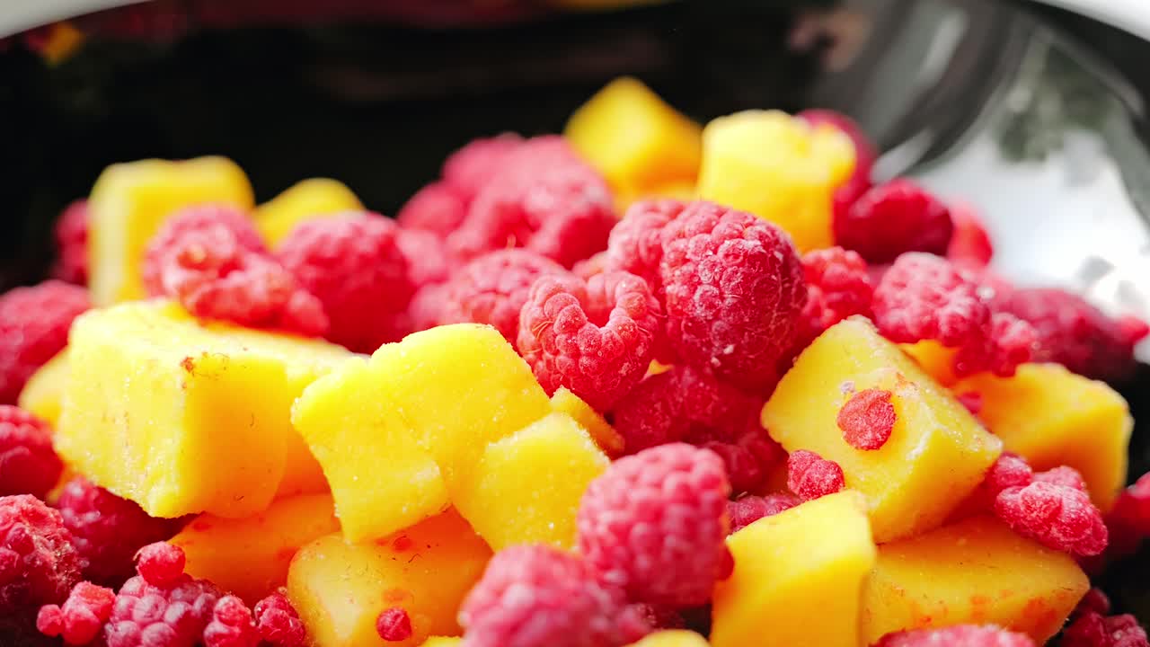 Close up of frozen raspberries and mango cubes shifted left inside black bowl