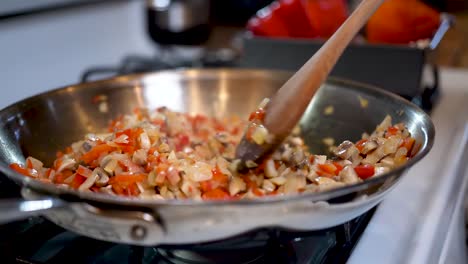 revolviendo una mezcla vegetariana de ingredientes en una sartén sobre la estufa - cámara lenta