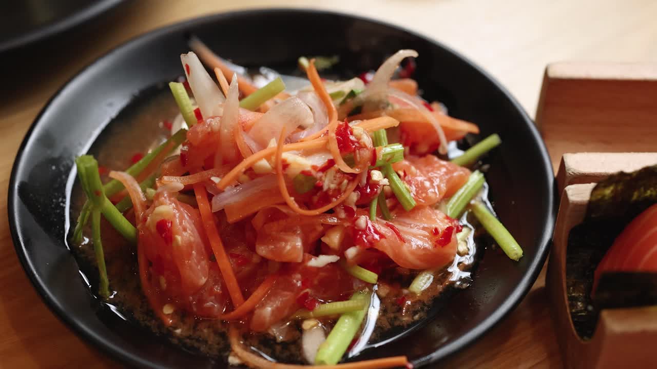Chopsticks stir raw salmon, vegetables, and chili in bright, natural light on wooden table