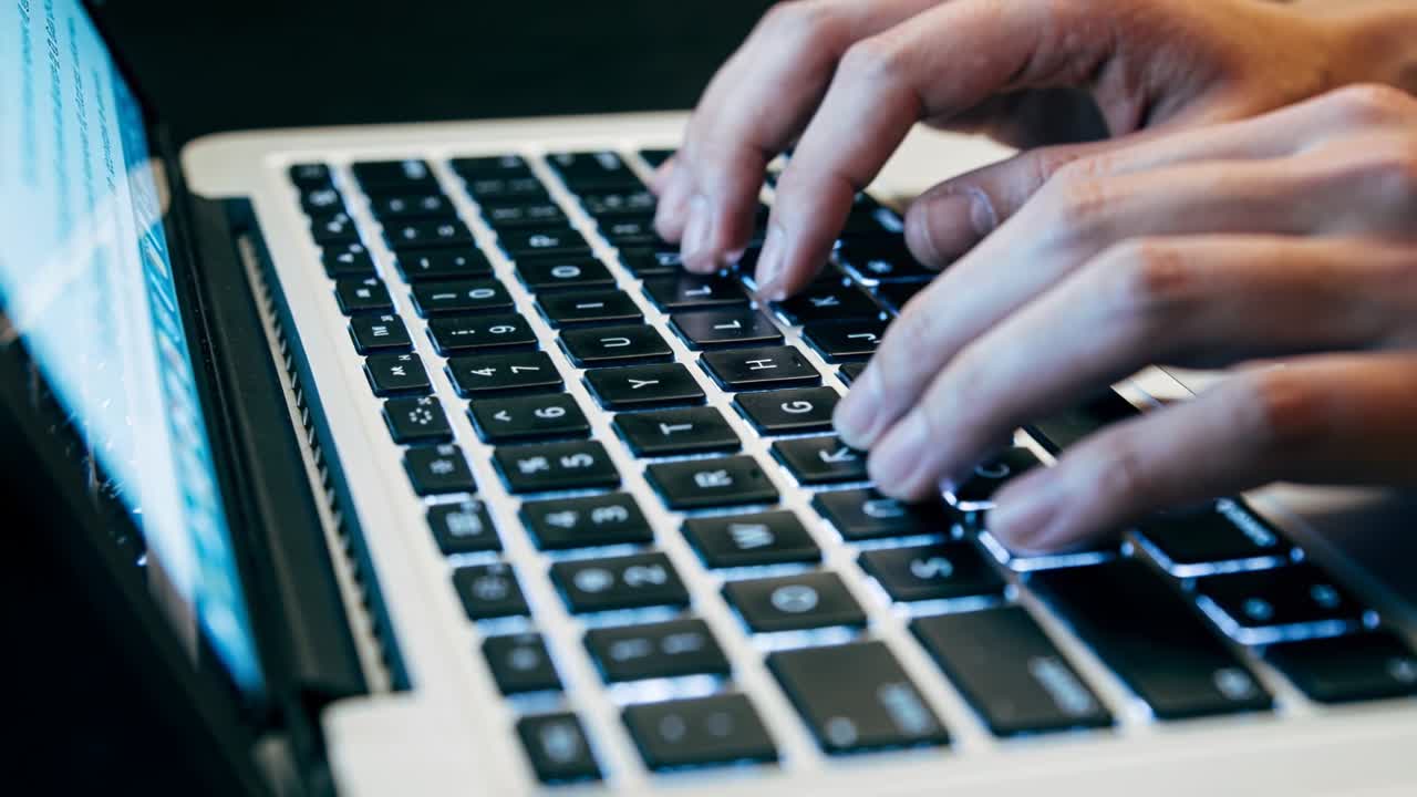 Fingertips starting, typing hands moving across backlit keyboard on laptop, entering blue code